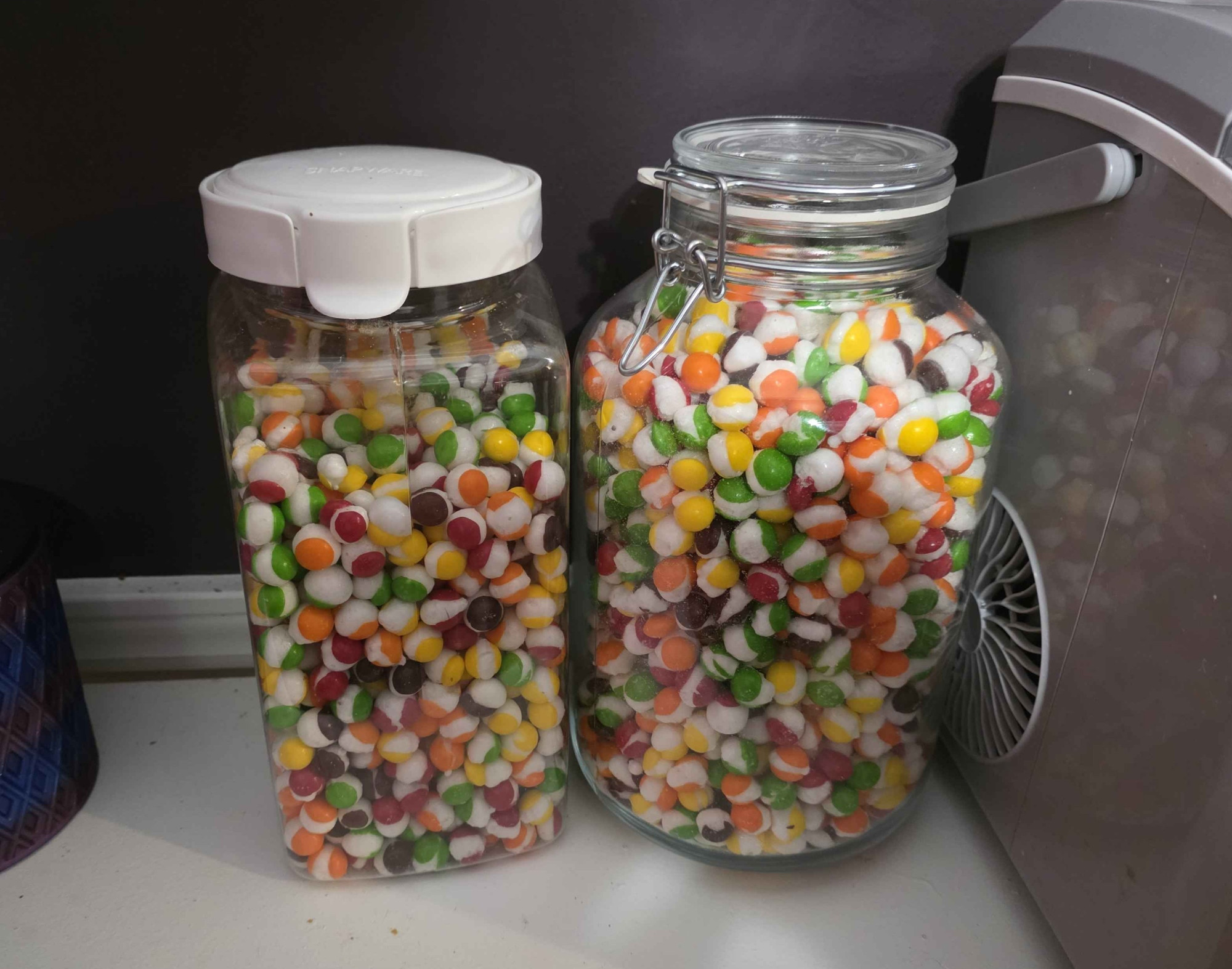 A photograph of two large containers full of freeze dried skittles.