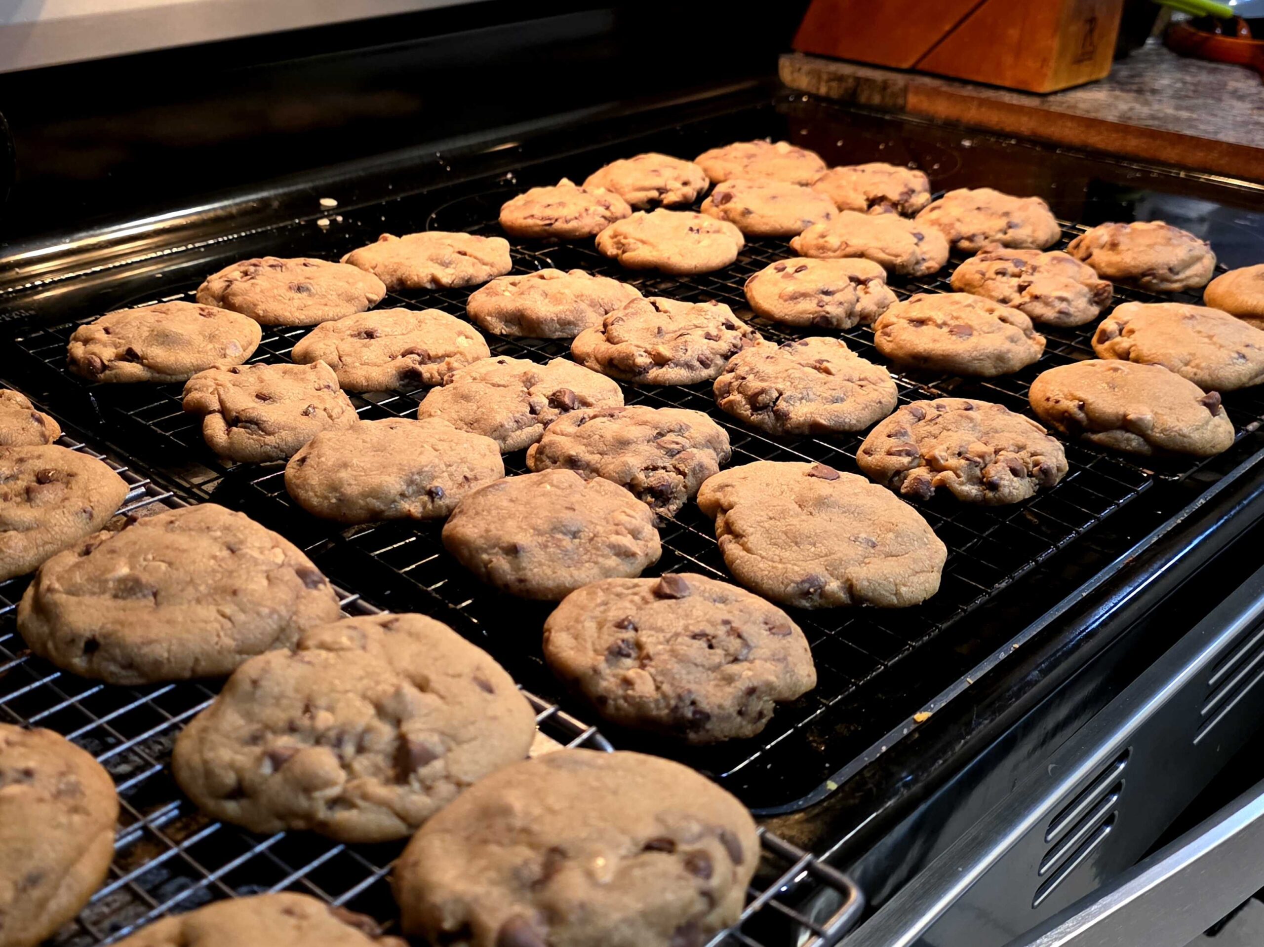 A close up of several cooling racks full of golden brown chocolate chip cookies. I wish my oven was clean but I'm a chaos entity.