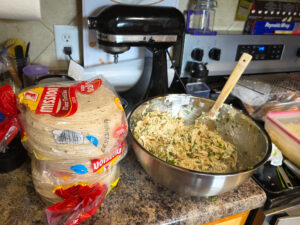 A giant bowl full of taquito filling next to a stack of tortillas